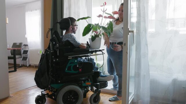 Personal assistant and a man with disability caring for a houseplant and enjoying its fragrance together at home.
