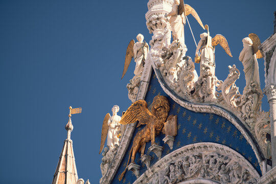 Gilded statues and ornate Gothic details stand out against the blue sky on the facade of St Mark's Basilica in Venice.