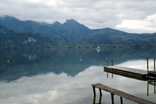 Wooden pier and distant ferry on calm alpine lake Kochelsee Germany for travel background