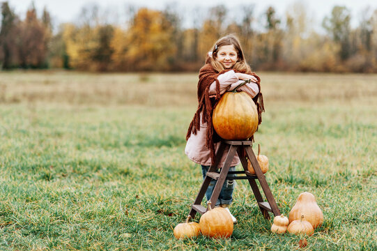 Happy little girl on pumpkin patch on cold autumn day, with a lot of pumpkins for Halloween or thanksgiving.
