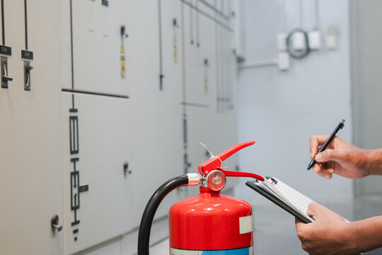 Engineer inspects fire extinguishers in the fire suppression control room, checking pressure levels to ensure safety in a factory or industrial setting.