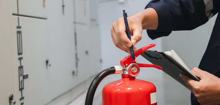 Engineer inspects fire extinguishers in the fire suppression control room, checking pressure levels to ensure safety in a factory or industrial setting.