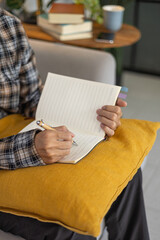 Fototapeta premium Close-up of a man writing in a notebook or journal on a sofa at home.