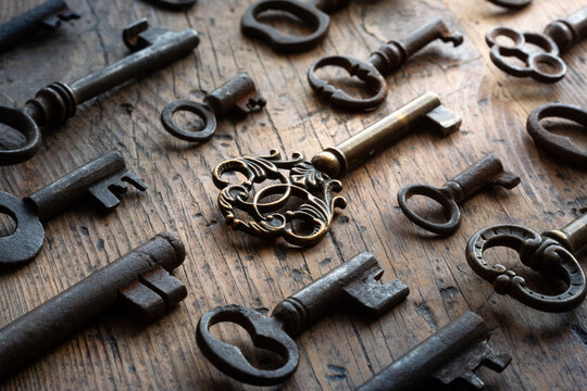 Collection of antique keys lying on a rustic wooden surface, with a dramatic beam of light highlighting the most ornate brass key. Atmospheric vintage still life evoking mystery, history.
