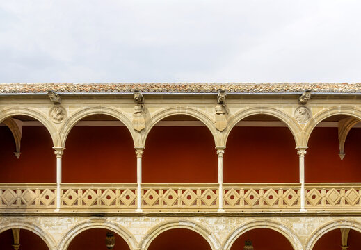 Casa de las Torres courtyard displaying an arcade with decorative columns and a carved stone railing, showcasing Renaissance Plateresque architectural details against a red wall