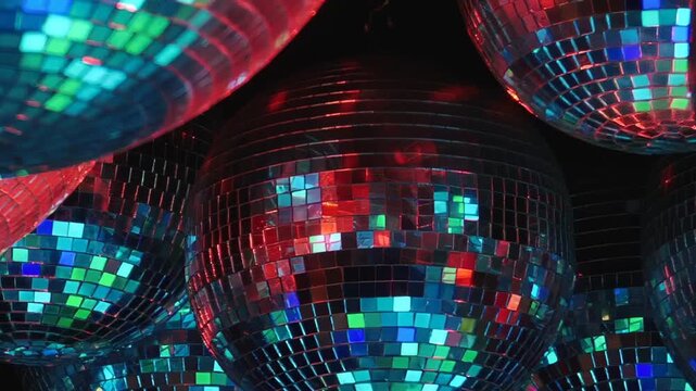 Clustered Mirror Balls Scatter Purple and Red Light. The grouped mirror balls fill the frame as mirrored mosaic surfaces catch changing colored light and form an abstract pattern.