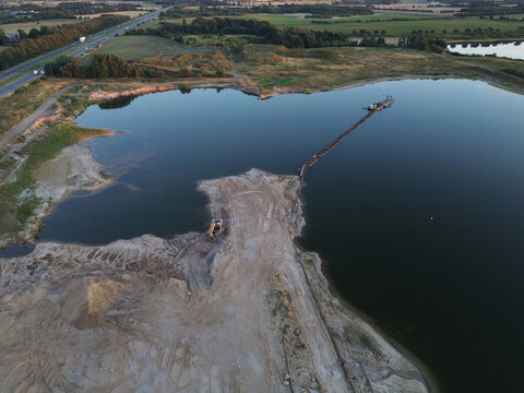 Aerial view of a floating suction dredger excavating sand and gravel underwater in a deep blue quarry lake surrounded by open pit landscapes on a sunny day