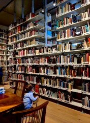 Little boy sitting on a wooden chair looking at high bookshelves in a library. © Тетяна Белаш