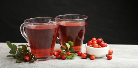 Hot rosehip tea in cups and berries with leaves on grey table, closeup © New Africa