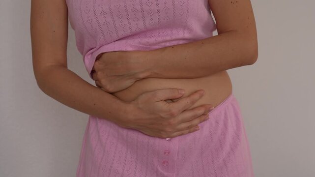 Young woman touches her stomach with both hands, illustrating abdominal pain, bloating or a possible pregnancy concept in a soft home lifestyle scene