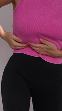 Young woman holds her right side, showing abdominal discomfort, cramps, gas, indigestion, muscle strain or possible appendix pain on a gray background