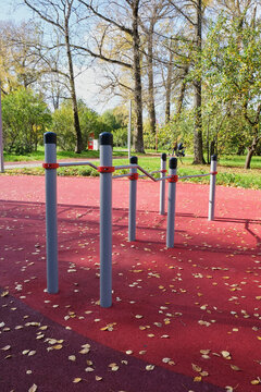 Outdoor Fitness Equipment and Calisthenics Bars on Red Rubber Surface in Park.