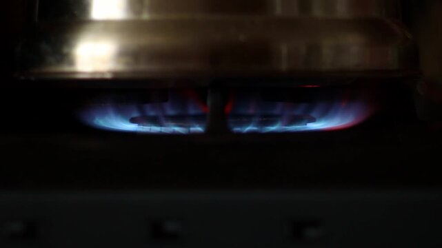 Horizontal close-up shot of a pot heating on a burning gas stove burner with blue flames in a kitchen. Cooking concept
