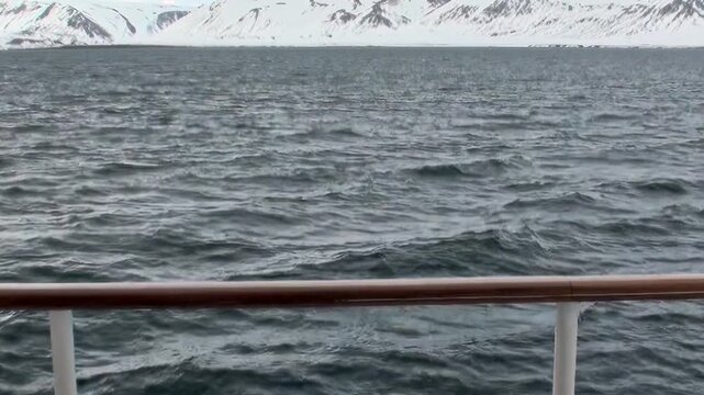 Arctic Ocean Ship Crossing Dark Polar Waters Across Open Water. Railing and deck elements frame the view while cold water stretches toward the distant polar horizon.