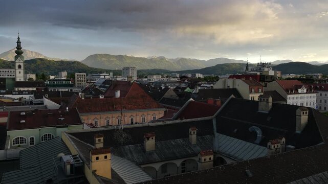 City rooftops of Klagenfurt are visible with mountains in the background as the sun sets.