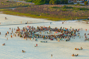 Obraz premium Large group of people gathered in a circle dancing and having fun on sandy beach at sea shore during summer vacations. Outdoor activities during travel time.