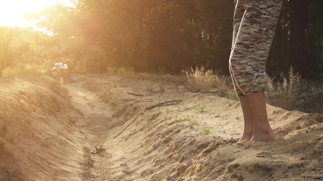 Girl in camouflage pants and pink T-shirt supports foot of sand. Slow motion. Evening time, sunset.