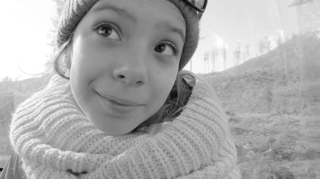 Little beautiful girl rides on a mountain lift, shows tongue and smiles.