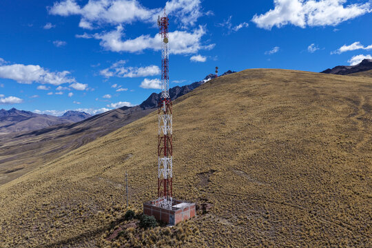 Red and white telecommunications tower on a hill of dry grass with a high Andean mountain range and blue sky behind