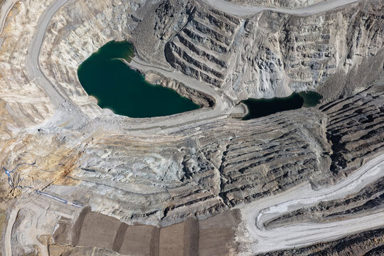 Open pit mine with stepped benches of light rock and two dark lagoons at the bottom of the pit during mine closure
