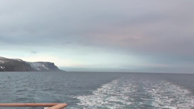Arctic Ocean Ship Gliding Across Cold Polar Sea Under Polar Sky. Dark swells move across the cold water while the distant polar horizon remains clearly visible.