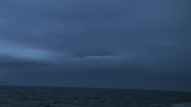 Arctic Ocean Ship Gliding Across Rolling Ocean Waters Under Arctic Sky. Dark swells move across the cold water while the distant polar horizon remains clearly visible.