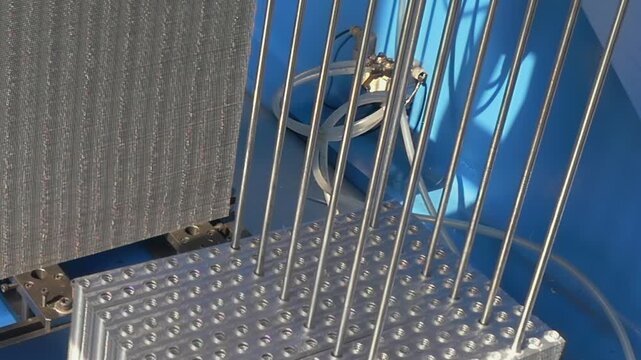 Precision robotic arms align thin silver pins into a structured grid pattern within a clean manufacturing facility during a productive morning session of automated assembly.