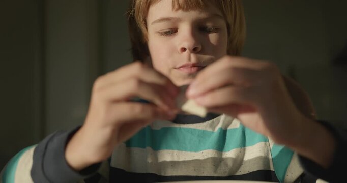 Close-up kid boy eats breakfast lunch in kitchen. 4K 10-bit