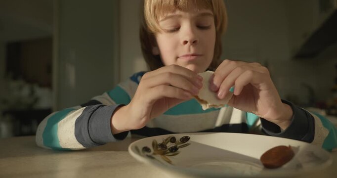 Close-up kid boy eats breakfast lunch in kitchen. 4K 10-bit