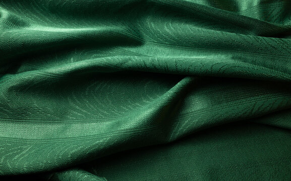 Close-up of emerald green textile with flowing folds, subtle woven pattern and soft highlights. Elegant abstract fabric background with rich texture.