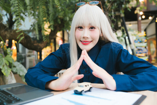 Happy young woman with blonde hair feeling joyful and successful holding small toy car model on desk for business strategy