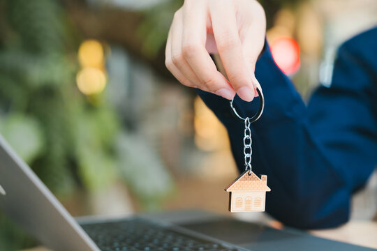 Real estate agent hand holding house key chain providing joyful service for property purchase transaction with laptop on office desk