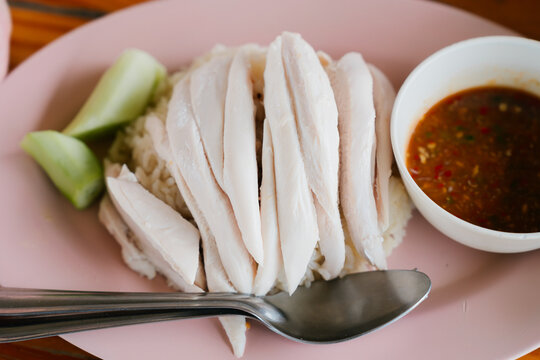 Steamed chicken rice dish served with flavorful dipping sauce and fresh cucumber, delicious meal creating sense of hunger and satisfaction
