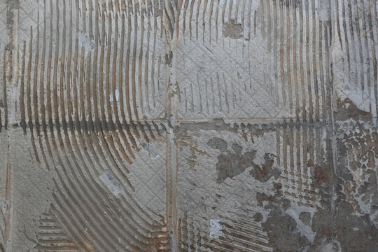 Old Tile Floor Removal Texture During Home Remodel. Close-up of an old floor during renovation showing exposed tile adhesive, mortar lines and worn subfloor texture after flooring removal.
