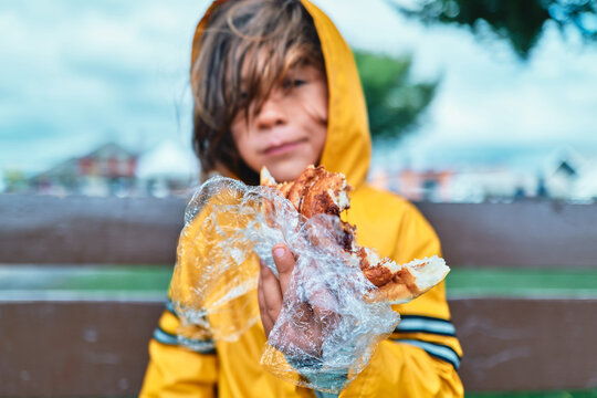 Boy in Yellow Raincoat Eating a Pastry on a Park Bench