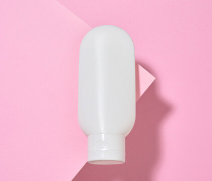 White plastic cosmetic tube on a pink background. Top view