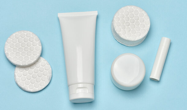 White tube, cotton pads on a blue background, top view, daily skin care and hygiene concept