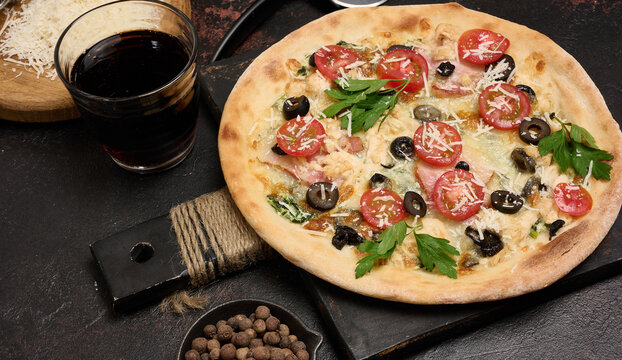 Whole pizza on a wooden board surrounded by tomatoes, olives, herbs, spices and kitchen tools