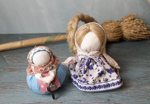 Two handmade cloth dolls in colorful patterned clothing displayed on a distressed wooden surface with natural straw craft elements in the background.