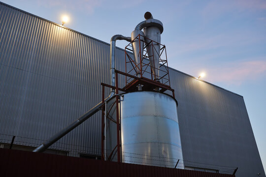Industrial dust collection system with cyclone separators, ductwork, exhaust equipment at a manufacturing facility. Industrial ventilation, particulate filtration equipment beside a metal-clad factory