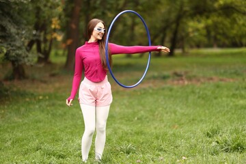 Athletic young woman exercising with hula hoop in park © New Africa
