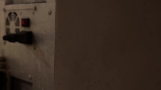 An outdated computer rests on a dusty surface in a dimly lit room, surrounded by shadows. The soft glow of a nearby light highlights the worn details and nostalgic charm of the device.