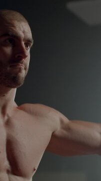 Focused shirtless athlete training in dimly lit gym, showcasing muscular upper body strength, intense concentration, and powerful physique during workout