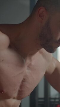 Focused muscular man training shirtless indoors, showcasing defined chest, shoulders, and intense athletic determination during a demanding strength workout session