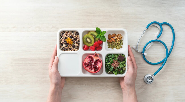 Healthy food divided into compartments in a container with a medical stethoscope balanced diet meal planning portion control dietary health
