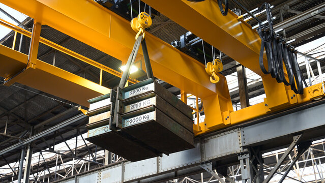 Overhead crane lifting heavy steel plates inside a metalworking factory, illustrating heavy industry, material handling, steel production and industrial work.