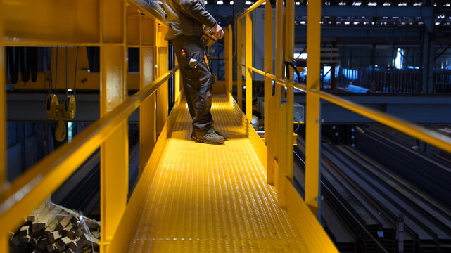 Industrial worker operating a remote control for an overhead crane in a steel factory, highlighting industrial technology, heavy machinery and metalworking.