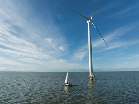 Sailboat Cruising Past Massive Wind Turbine in IJsselmeer