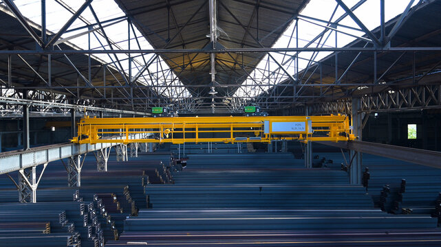 Overhead bridge crane spanning a large steel storage facility, showcasing heavy industrial infrastructure, steel inventory, material handling and manufacturing operations.