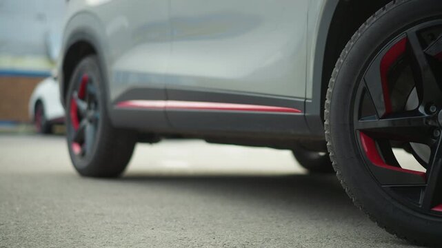 Close up view of car front left wheel with black finish and distinctive red accents focusing on tire tread details. camera smoothly tracks vehicle as it moves forward in outdoor parking area